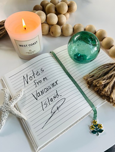 Open notebook handwritten with Notes from Vancouver Island, beside a West Coast candle, glass float, wooden beads, and a starfish